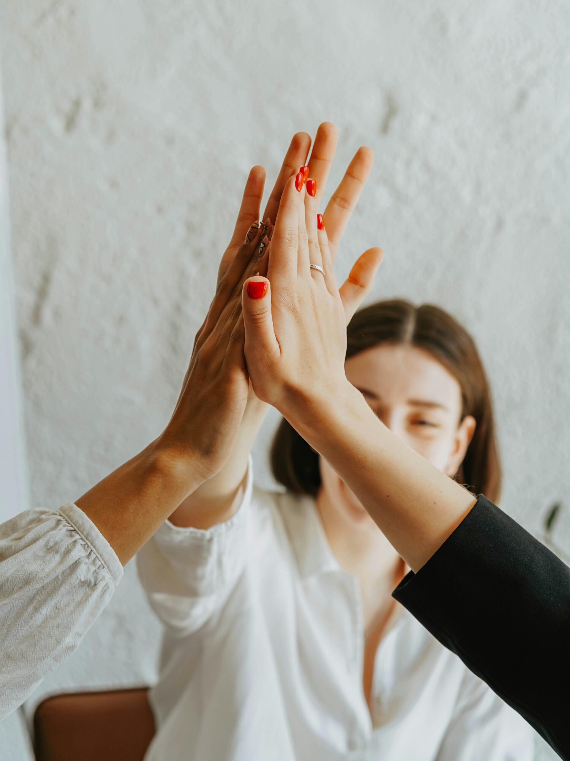 A group of adults in a warm atmosphere celebrating teamwork with a high-five gesture.